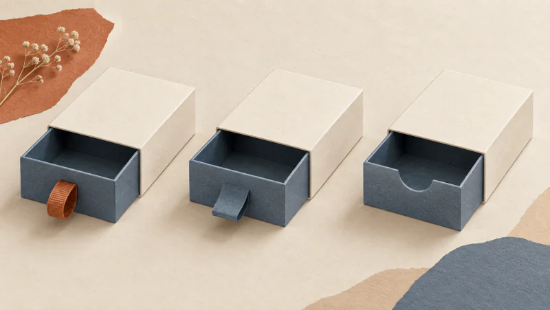 Three drawer boxes using a ribbon loop, an integral paper tab and a finger recess for opening.