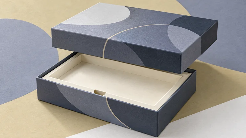 Editorial collage of a printed rigid gift box with its lid raised above a fitted paperboard insert.
